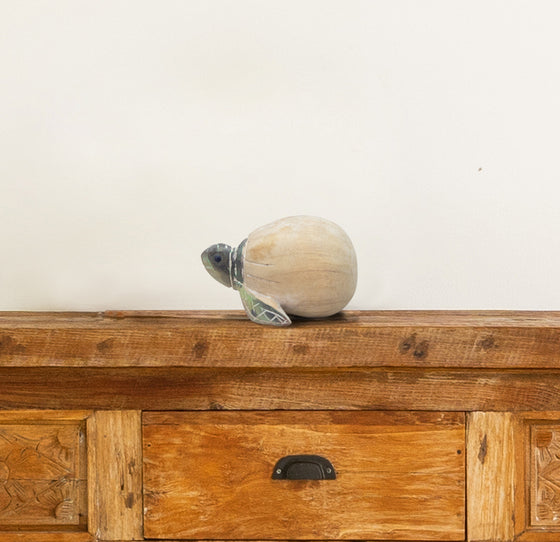 wooden green turtle partially outside of a beige egg sitting on top of a dresser